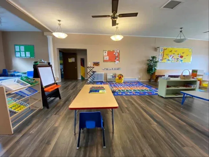 An open room with a ceiling fan, an easel, a small table and chair, and a carpet in the far corner.