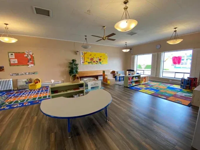 A wide room with a curved table, a cosy corner with a small armchair, two carpets and big windows.